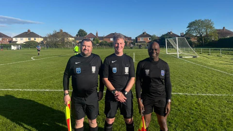 Three Chester match officials standing together on a local football pitch